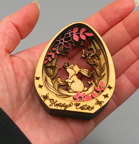 small Happy Easter layered wood egg decoration with a bunny, butterflies, and flowers shown in woman's hand for relative size